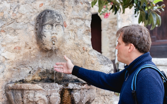 Man interacting with historical stone fountain in Eze, France.