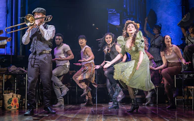 Stage performance of Hadestown in West End with actors singing and dancing.