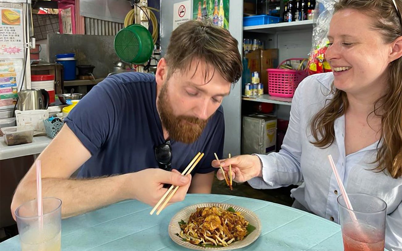 Tourists enjoying local cuisine with chopsticks during a food tour in George Town.