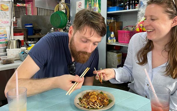 Tourists enjoying local cuisine with chopsticks during a food tour in George Town.