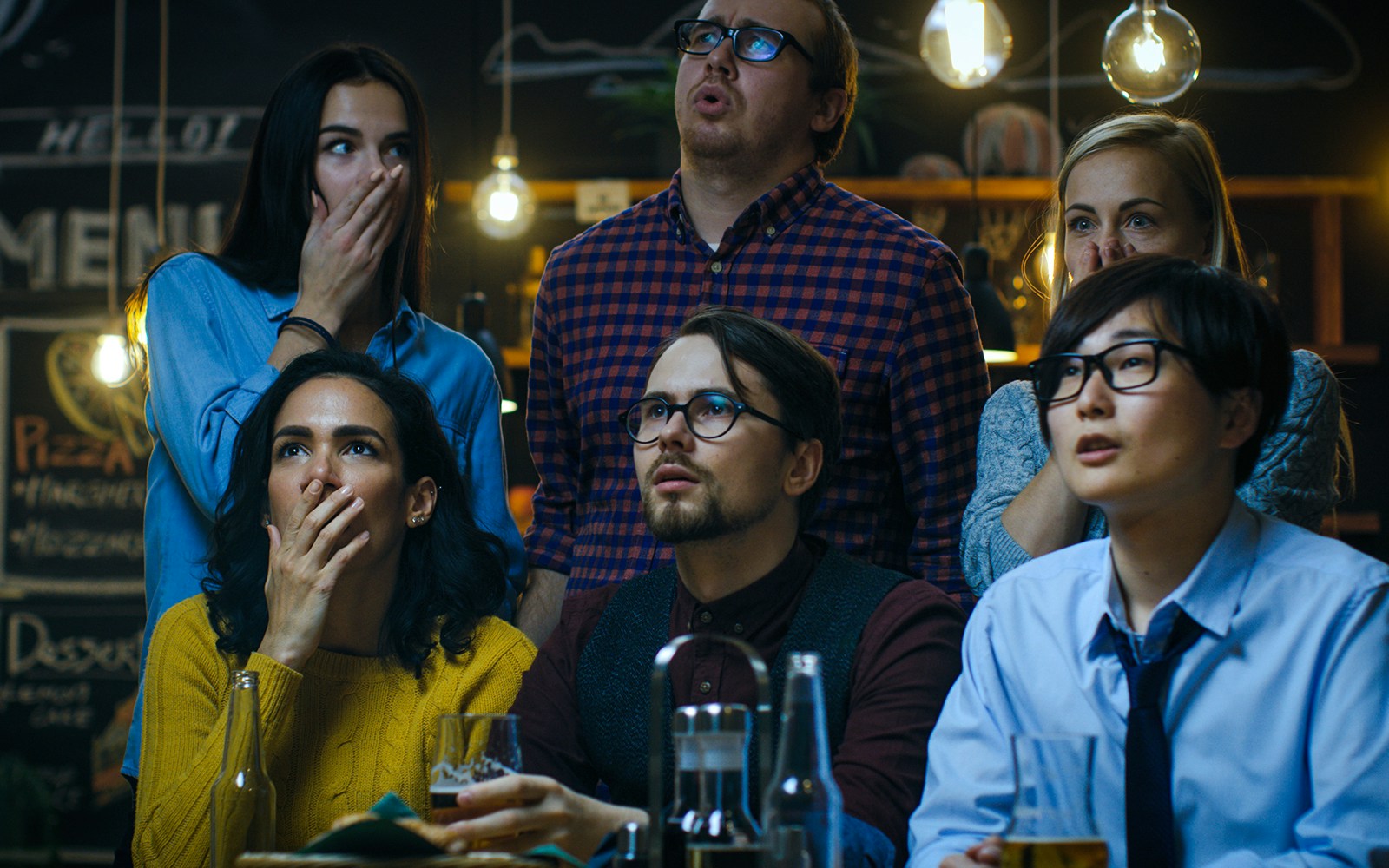 Young people in a bar listening intently to horror stories, expressions of surprise and intrigue.