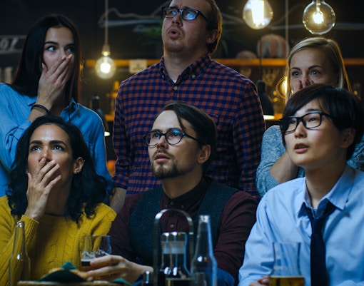 Young people in a bar listening intently to horror stories, expressions of surprise and intrigue.