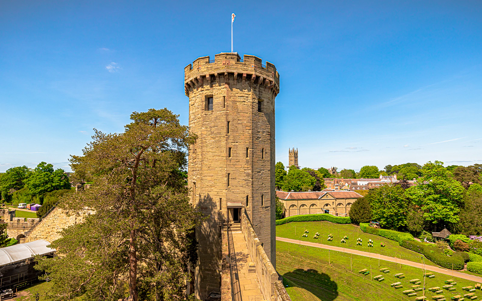Warwick Castle's Dragon Tower with surrounding gardens and distant church.