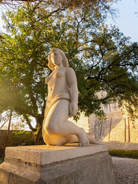 Statue of a woman at Sao Jorge Castle, Lisbon, with trees and castle wall in the background.