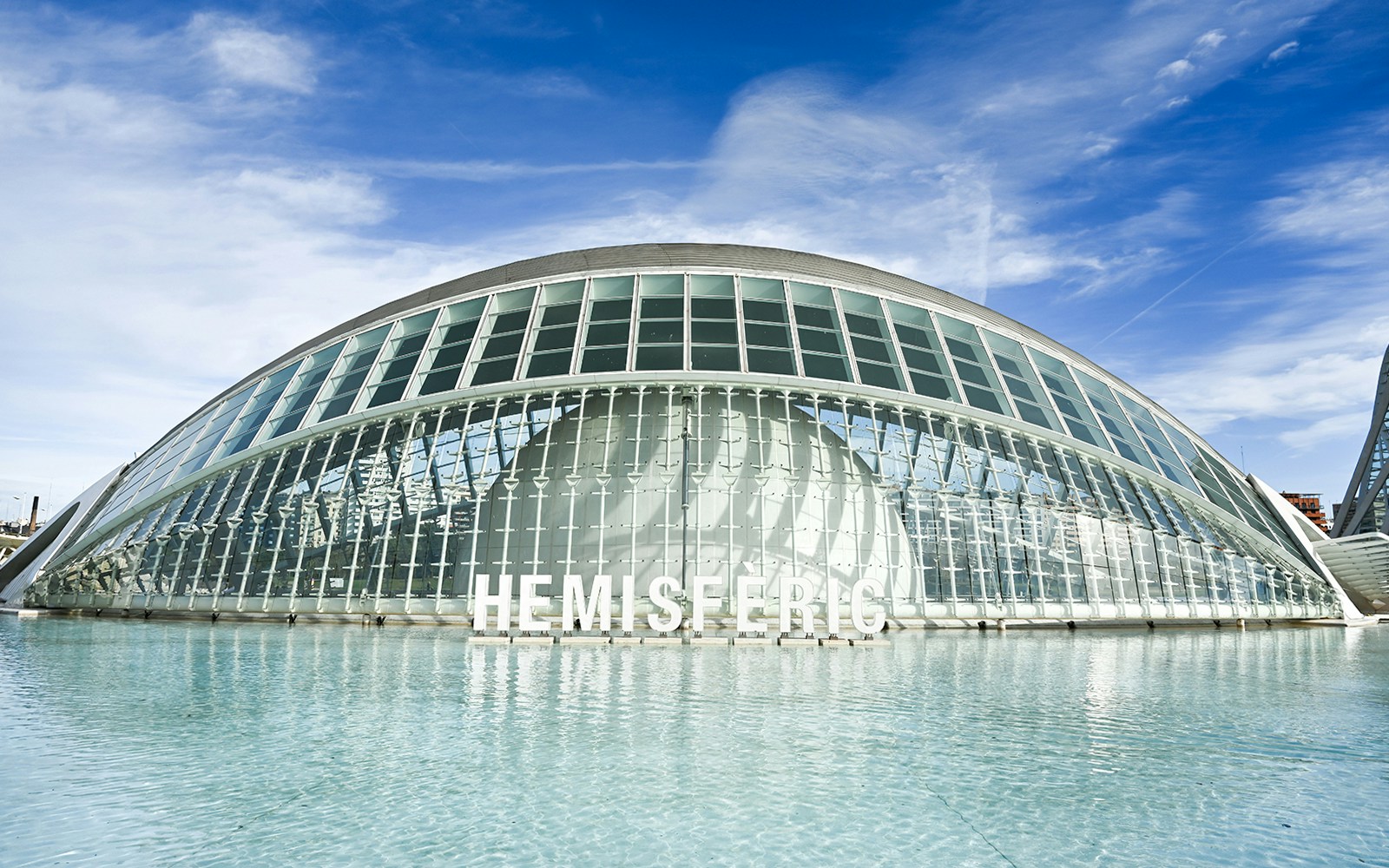 Hemisferic building with glass facade reflecting in water, Valencia, Spain.