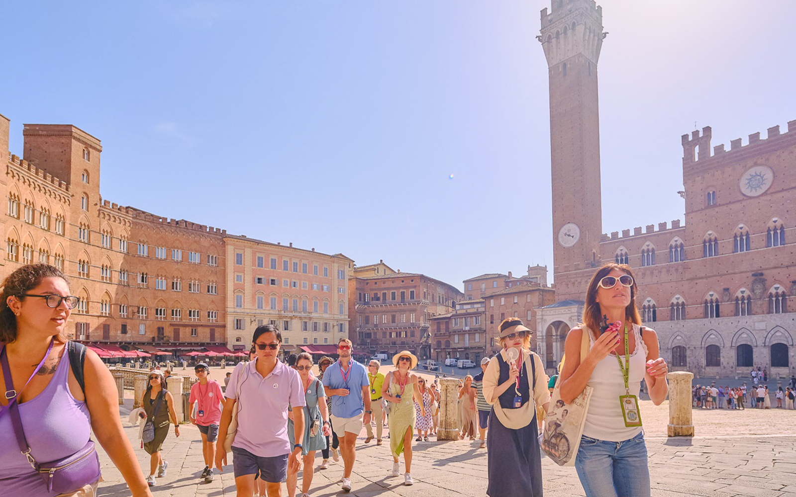 Tour group with guide at Piazza del Campo, Siena, Italy, with historic buildings in background.