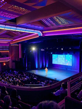 Performer on stage at Sydney Comedy Festival show in a vibrant theater setting.