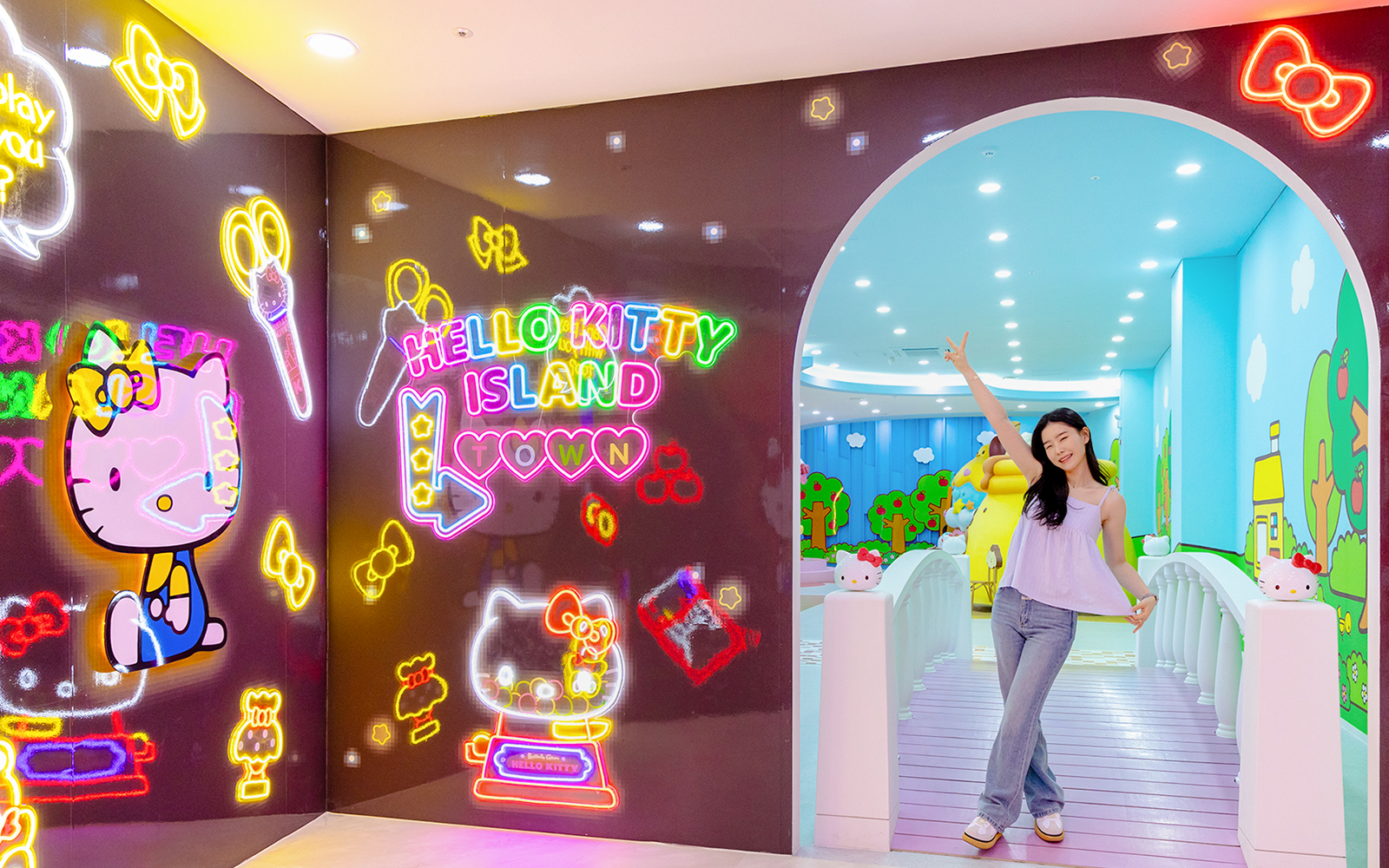 Tourist posing at Hello Kitty Island entrance with neon signs and colorful decor.