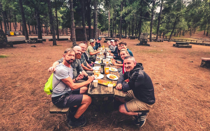 Group enjoying local food at a picnic table in a forest during Gran Canaria volcano sunset tour.