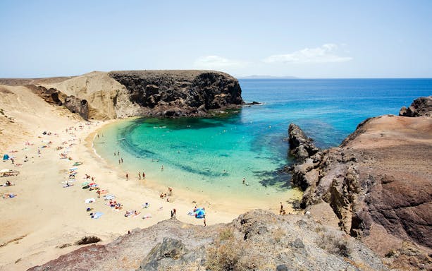 Beachgoers at Papagayo Beach, Lanzarote, with clear turquoise water and rocky cliffs.