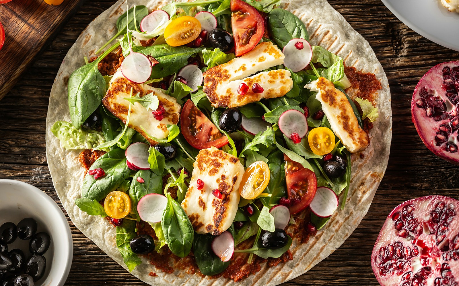 Vegetarian tortilla with radish, cherry tomatoes, olives, pomegranate, and grilled halloumi cheese.