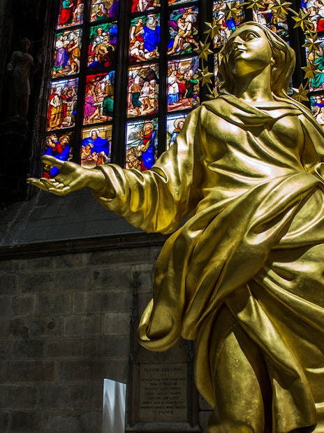 Golden statue inside Milan Cathedral with stained glass windows in the background.