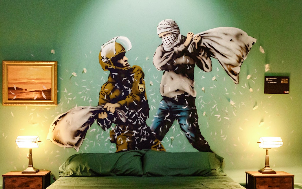 Street art mural of a pillow fight in the Banksy Museum room, featuring a soldier and a masked figure.