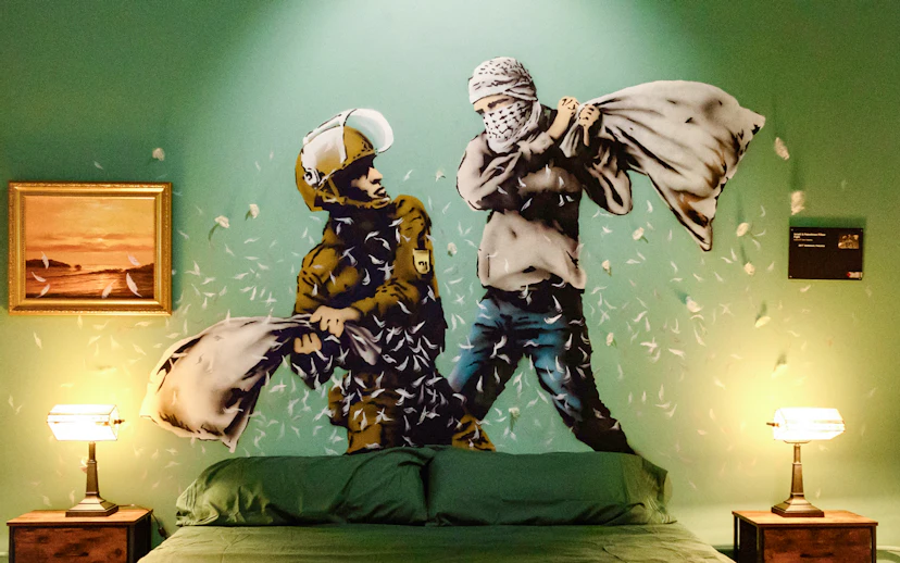 Street art mural of a pillow fight in the Banksy Museum room, featuring a soldier and a masked figure.