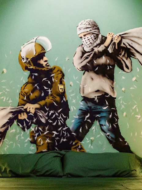 Street art mural of a pillow fight in the Banksy Museum room, featuring a soldier and a masked figure.