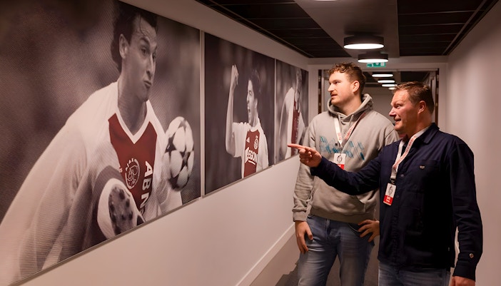 Visitors observing football player photos at Johan Cruijff ArenA tour.