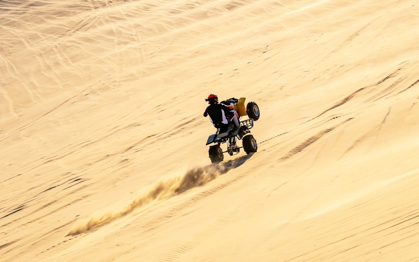 Man performing quad bike stunt on sand dunes in Doha.