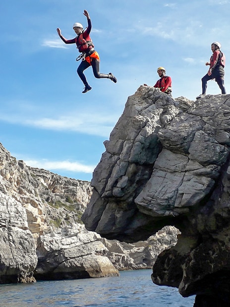 Coasteering participants jumping from rocky cliffs into the sea.