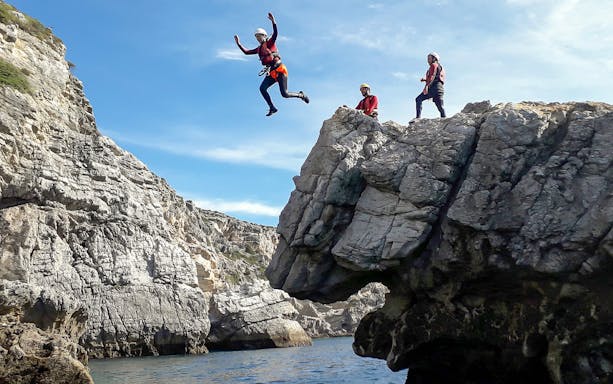 Coasteering participants jumping from rocky cliffs into the sea.