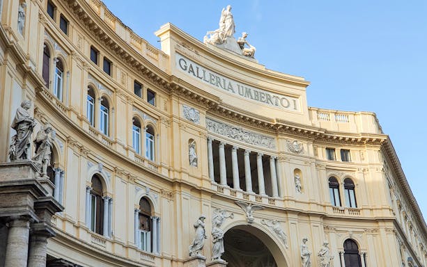 Galleria Umberto I facade in Naples, Italy, featuring classical statues and architectural details.