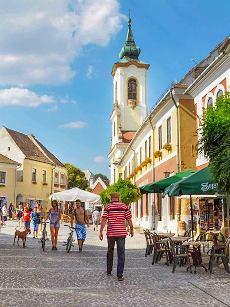 Guests walking through Szentendre's medieval old town with colorful buildings and a church tower.