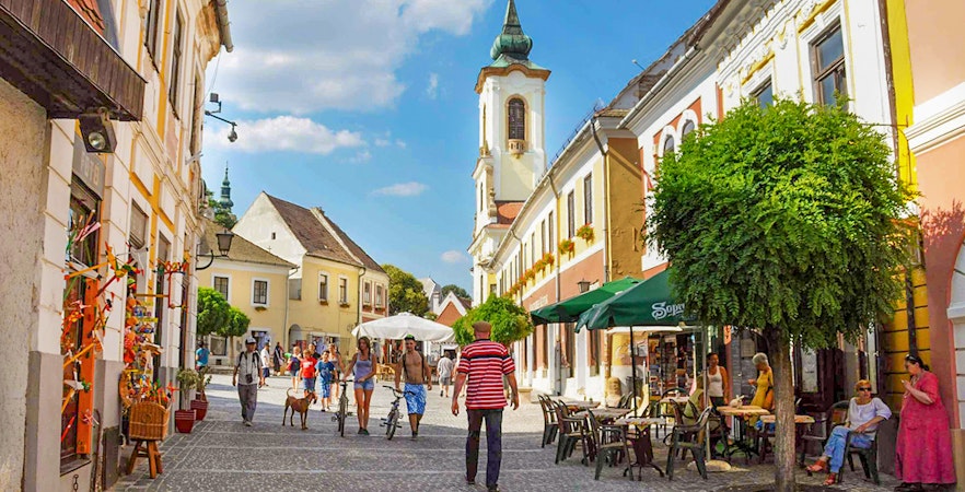 Guests walking through Szentendre's medieval old town with colorful buildings and a church tower.