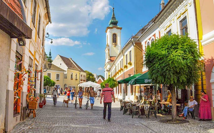 Guests walking through Szentendre's medieval old town with colorful buildings and a church tower.