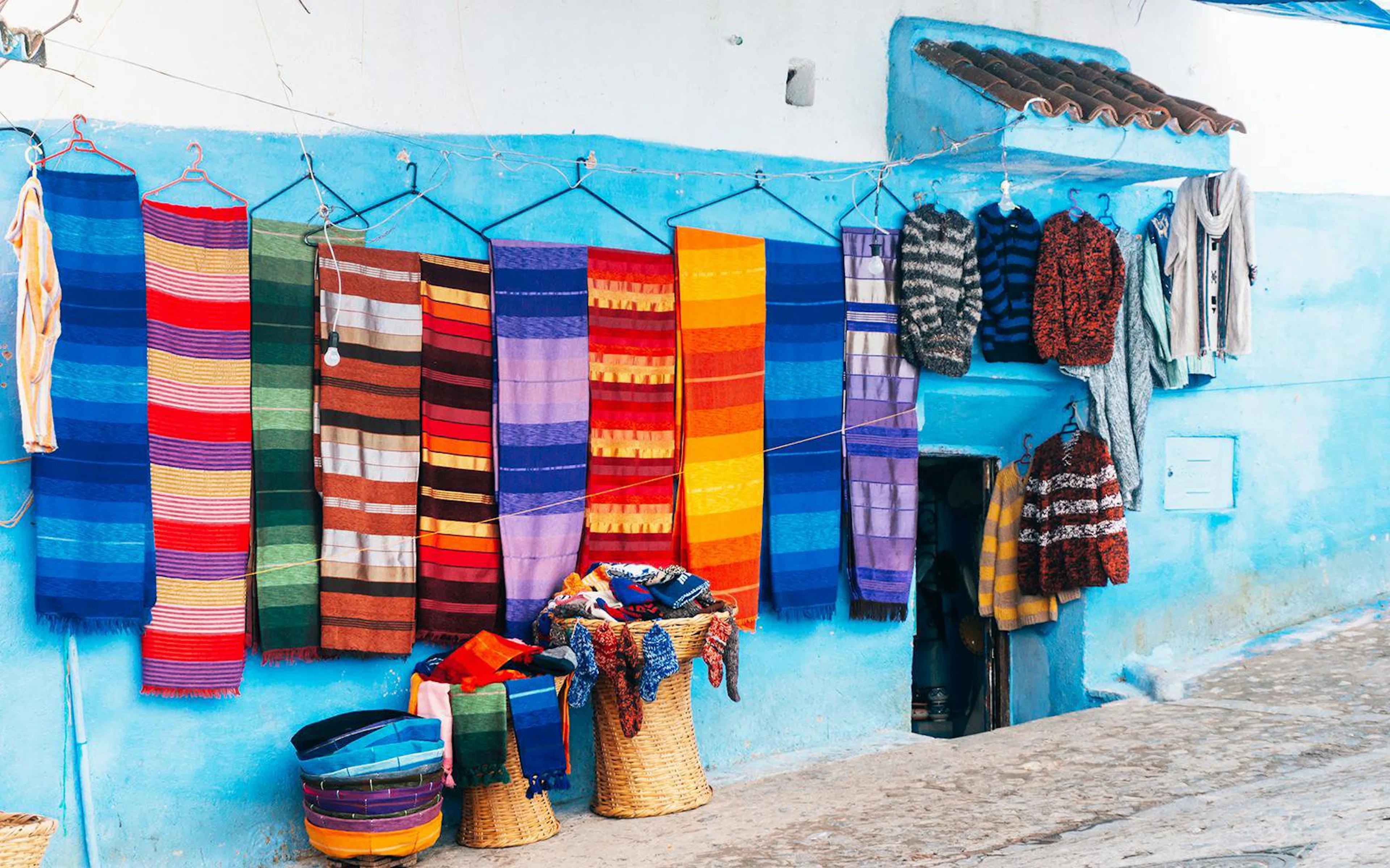 Colorful textiles and garments hanging on a blue wall in Chefchaouen, Morocco.