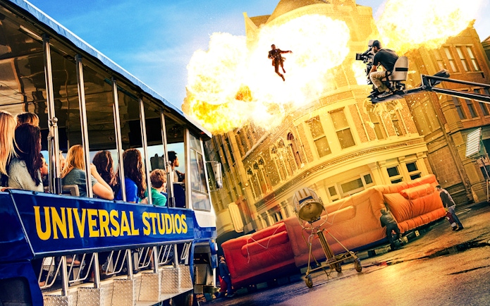 Universal Studios Hollywood tram tour with guests watching a movie stunt explosion scene.