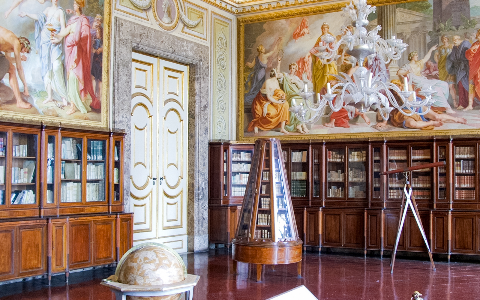 Royal Palace of Caserta library with ornate ceiling frescoes and wooden bookcases.