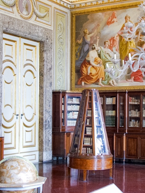 Royal Palace of Caserta library with ornate ceiling frescoes and wooden bookcases.
