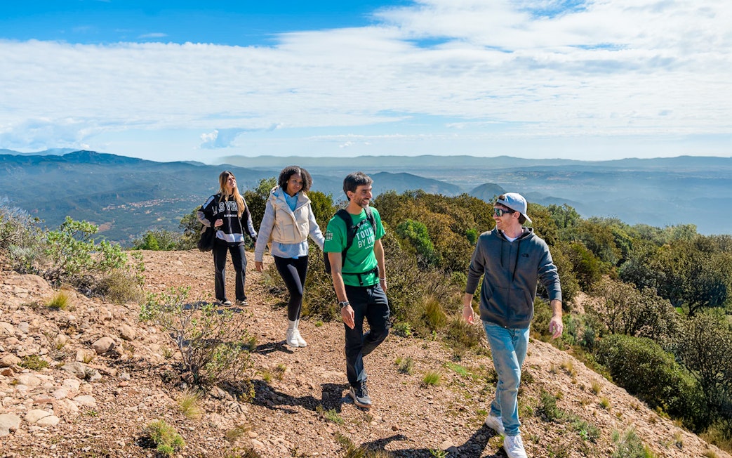 Tourists hiking with guide on Montserrat mountain trail with scenic views.