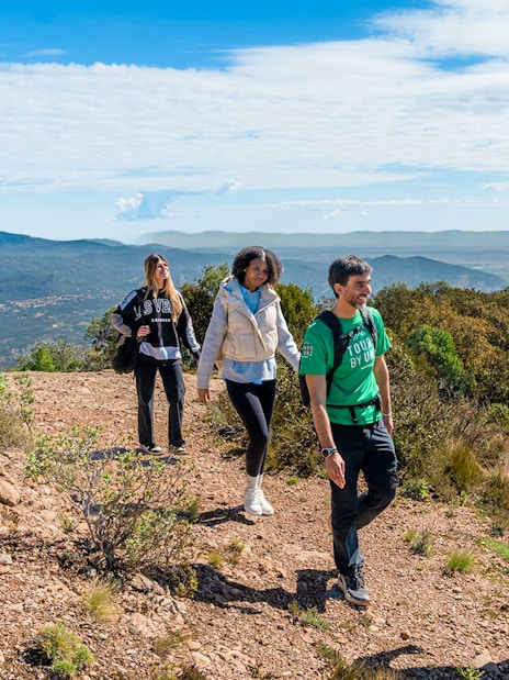 Tourists hiking with guide on Montserrat mountain trail with scenic views.