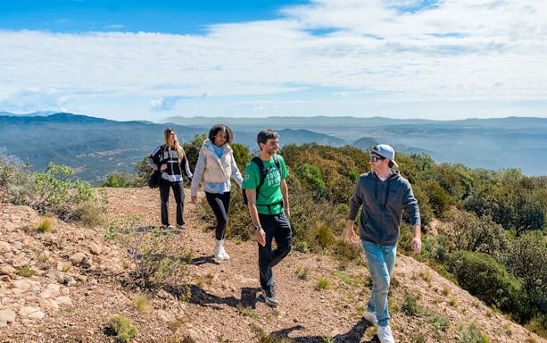 Tourists hiking with guide on Montserrat mountain trail with scenic views.