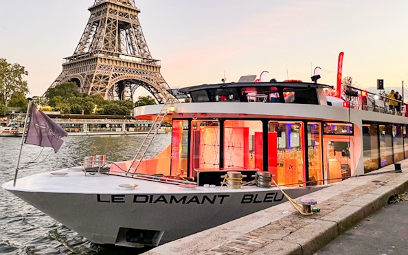 Le Diamant Bleu cruise boat docked on Seine River with Eiffel Tower in background.