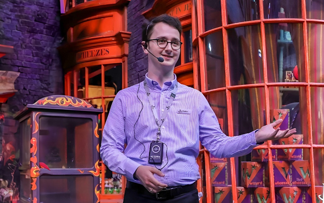 English-speaking guide presenting at a themed attraction with colorful storefronts.