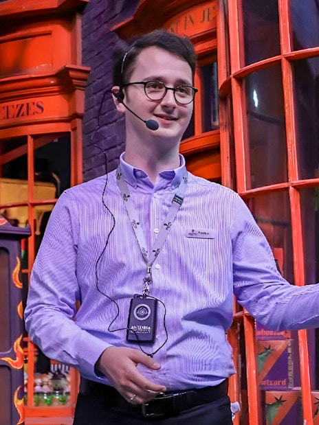 English-speaking guide presenting at a themed attraction with colorful storefronts.