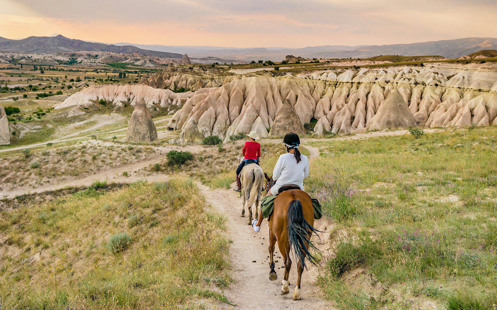 Horseback riders on a trail in Goreme, Cappadocia, with unique rock formations in the background.
