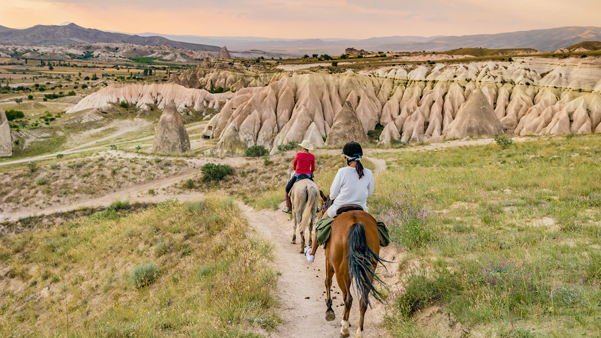 Horseback riders on a trail in Goreme, Cappadocia, with unique rock formations in the background.