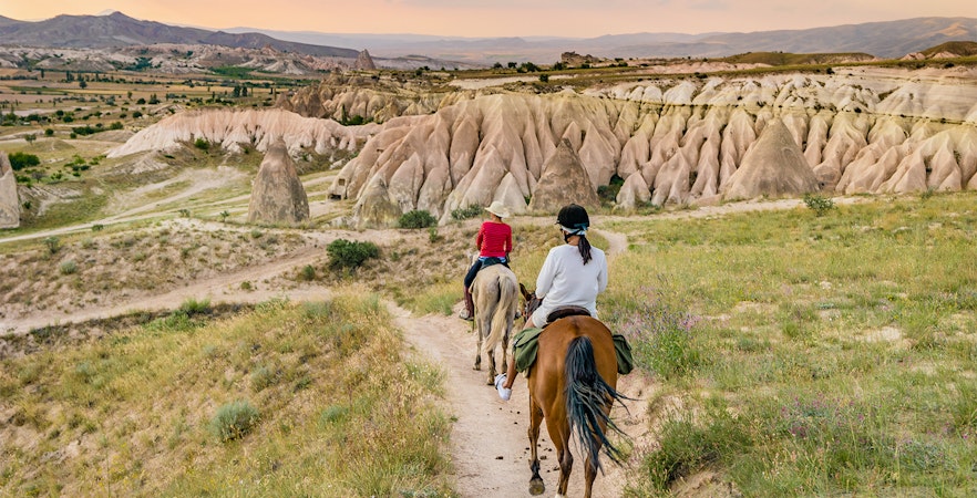 Horseback riders on a trail in Goreme, Cappadocia, with unique rock formations in the background.