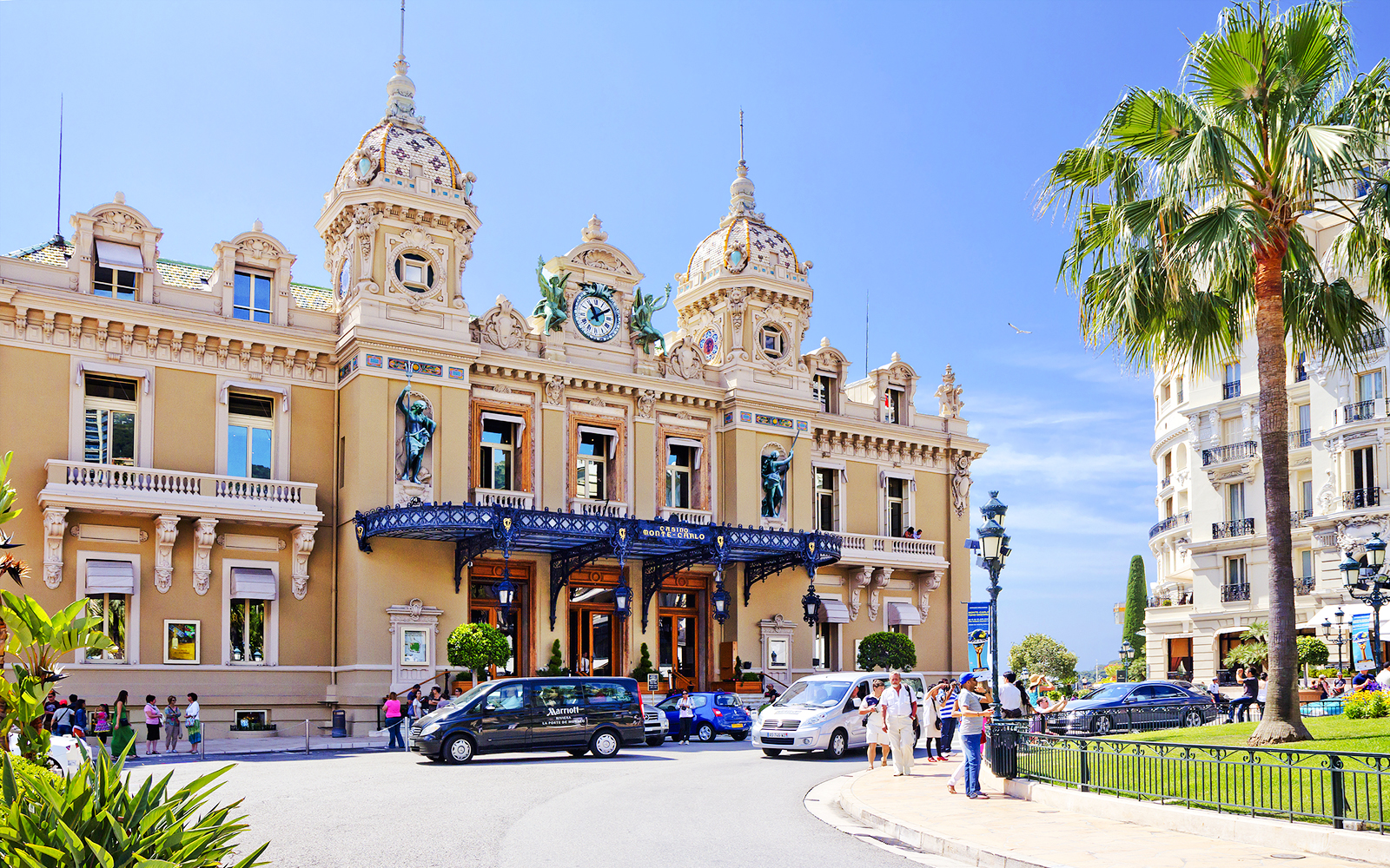 Monte Carlo Casino entrance with visitors and parked cars in Monaco.