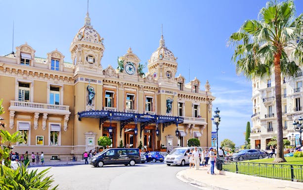 Monte Carlo Casino entrance with visitors and parked cars in Monaco.