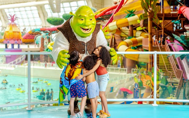 Kids hugging a character at DreamWorks Water Park with colorful slides in the background.