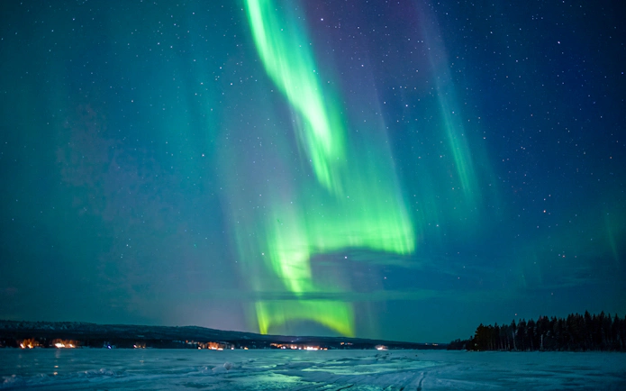 Northern lights over snowy landscape in Rovaniemi with starry sky.