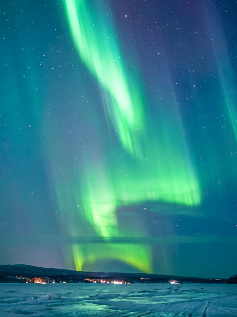 Northern lights over snowy landscape in Rovaniemi with starry sky.