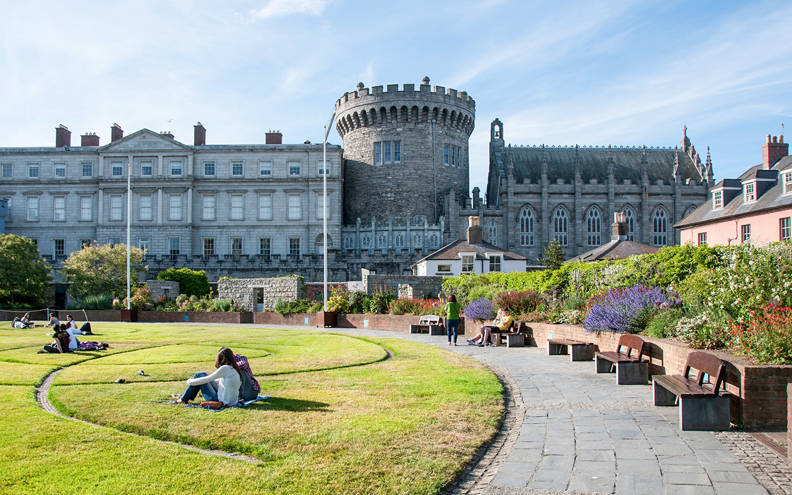 Dublin Castle gardens with people relaxing on the lawn and benches.