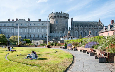Dublin Castle gardens with people relaxing on the lawn and benches.