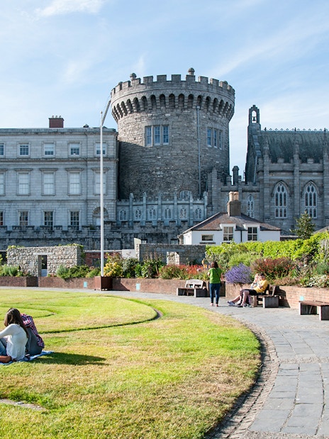 Dublin Castle gardens with people relaxing on the lawn and benches.