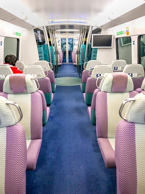 Interior of Hong Kong Airport Express train with purple seats and passenger.