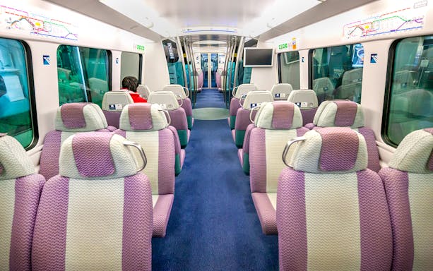 Interior of Hong Kong Airport Express train with purple seats and passenger.